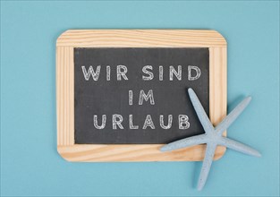 We are on vacation is standing in german language on the chalkboard with a sea star, holiday