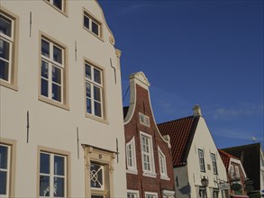 Close-up of various house facades with white and brick fronts under a cloudless sky, greetsiel,