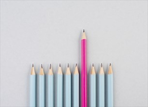 Blue pencils in a row, one pink pen is standing out, be different, leadership and teamwork concept