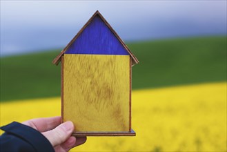 Holding a house in the hand with the colors of the ukrainian flag, home for refugees from Ukraine,