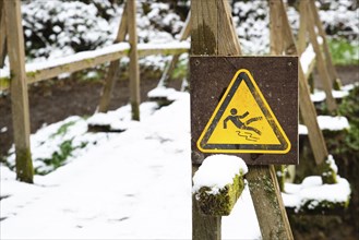 Slippery warning sign in the forest, wooden bridge covered with snow, winter season, beware of