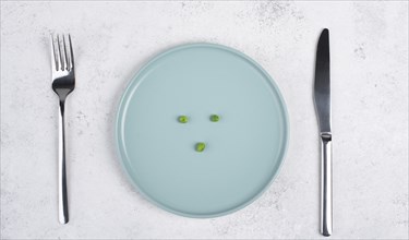 Three green peas on a plate, fork and knife on the table, diet and loosing weight concept, healthy