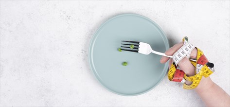 One single pea on a plate, hand with tape measure and fork, diet and loosing weight concept,