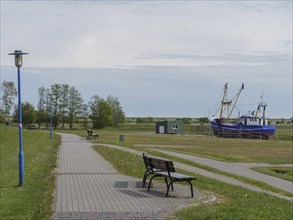 A park path with benches leads along a rural setting with fishing boats in the background,
