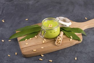 Pesto made from wild garlic, pine nuts and feta cheese in a glass, with fresh leaves on a dark