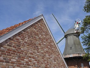 Brick building with the top of a windmill in the background under a blue sky, Greetsiel, East