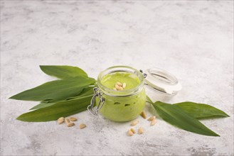 Pesto made from wild garlic, pine nuts and feta cheese in a glass, with fresh leaves on a textured