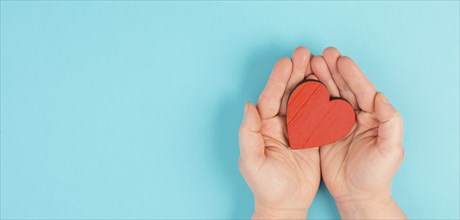 Woman is holding a red heart in her hand, blue colored background, copy space, love and charity