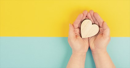 Woman is holding a heart in her hand, blue and yellow colored background, copy space, love and