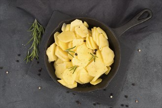 Sliced potatoes in a pan with rosmarine, pepper and olive oil, healthy vegetarian food