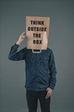 Young men has a paper bag on his head, the phrase think outside the box is standing on it,