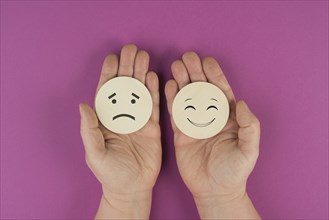 Holding two wooden circles in the hands one face is sad the other one is smiling, positive and