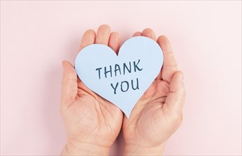 Holding a heart with the words thank you in the hands, pink colored background, greeting card,