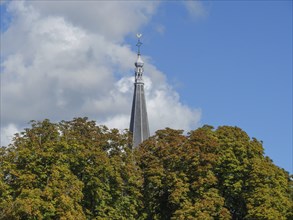 Close-up of a tall church tower rising above the leafy trees under a cloudy sky, Doesburg,