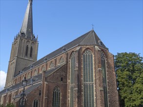 Large Gothic church with high windows and a steep bell tower, in sunny weather with a blue sky,