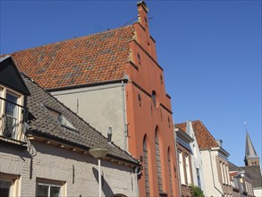 Row of historic buildings with tiled roofs and windows along a quiet street under a clear blue sky,