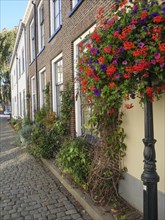 Narrow street with planted house fronts and blooming flowers on a lantern, Brick houses and