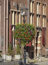 A colourful display of flowers hanging from a lamppost in front of a historic brick building with