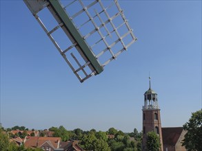 Parts of a windmill and a church tower rise above the roofs of a quiet village, Ditzum,