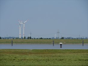 In the distance, wind turbines stand on a wide meadow under a cloudless sky, Ditzum, rheiderland,