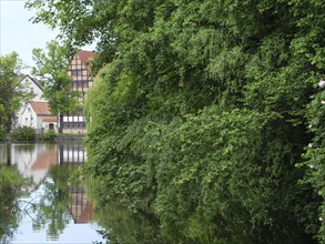 Tranquil lake with reflections of half-timbered houses and trees, surrounded by lush nature,