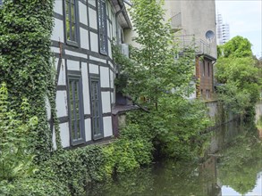 Half-timbered house on the banks of a quiet river, surrounded by dense green foliage, Detmold,