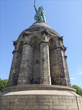 Massive monument with a statue on a stone pedestal under a clear blue sky, Detmold, North