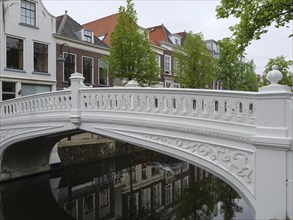 Decorative white bridge over a canal, surrounded by houses and green trees, Delft, Holland,