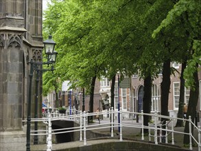 Historic buildings on a bridge over a canal, surrounded by green trees and lanterns, Delft,