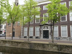 An old, historic brick building with many windows and trees, next to a quiet canal, Delft, Holland,