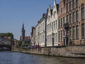 Historic buildings and a church tower along a canal with detailed architecture and blue sky,