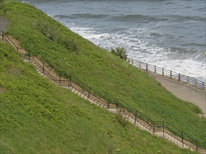 Path along a green coastline with steps and railings. View of the rough sea, Thynemouth, England,