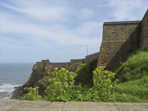 Historic cliffs on the coast with walls running over them, leaning towards the sea, under a cloudy