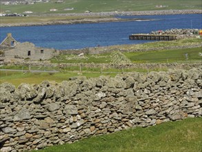 Ancient stone ruins and a stone wall in a green coastal landscape by the sea, lerwick, shetlands,