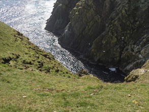 Steep cliffs and the sea in the sun with waves crashing against the rocks, lerwick, shetlands,