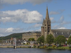 Large church tower and municipal buildings next to a bridge over a river with blue sky and clouds,