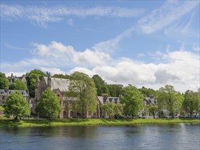 View of a picturesque row of houses and a church along a river with blue sky and white clouds,