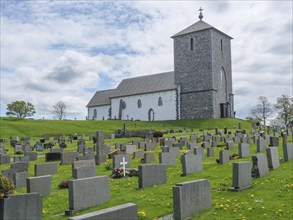 A small church with a multitude of gravestones on a green meadow under a cloudy sky, haugesund,
