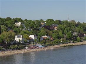 Spacious beach by the water with trees and buildings in the background, relaxed atmosphere, Elbe,