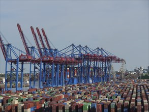 Large container cranes in the harbour, many stacked containers in different colours and ships in