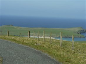 Road leading along a wooden fence overlooking a green island in the sea, lerwick, shetlands,