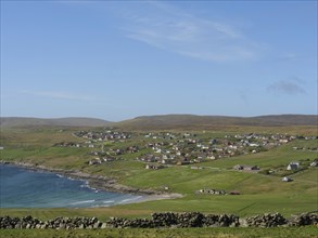 A coastal village scene with green fields and scattered houses under a clear sky, lerwick,