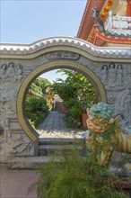 A decorative stone arch with a sculpture of a lion in a traditional temple garden with surrounding