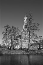 Black and white picture of a historic castle with trees and moat, cold and calm atmosphere,