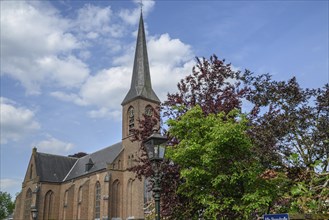 Brick church with high steeple and clock, surrounded by trees under a blue sky, creates a peaceful