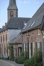 A peaceful village street with a view of the church tower, surrounded by old brick houses, planted