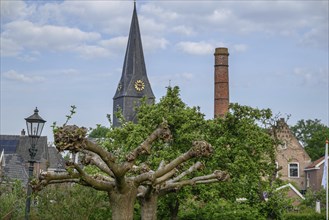 Quiet village scene with a high church tower, an old chimney and green trees in sunny weather,