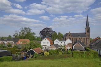 A church and various houses in a green village, accompanied by trees and a cloudy sky, Bredevoort,