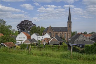 Village view with a church in the background, surrounded by houses, a meadow and trees under a