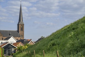 Rural scene with a church in the background, a steep green hill and quiet houses in sunny weather,